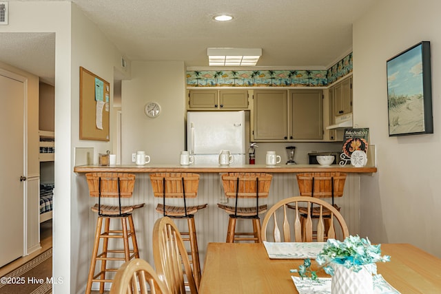 kitchen with under cabinet range hood, visible vents, a peninsula, a textured ceiling, and freestanding refrigerator