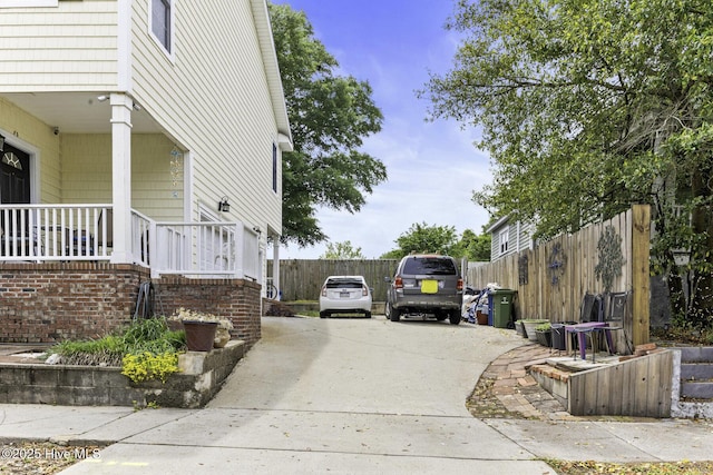view of property exterior featuring concrete driveway, covered porch, and fence