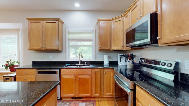 kitchen featuring dark stone counters, light wood finished floors, a sink, and appliances with stainless steel finishes