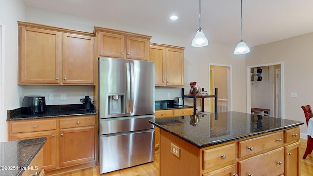 kitchen with dark stone countertops, stainless steel refrigerator with ice dispenser, light wood-style floors, and pendant lighting