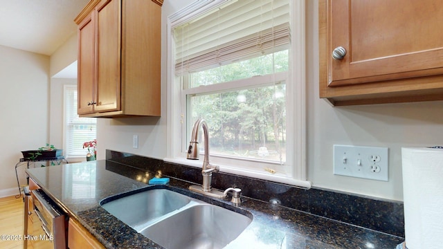 kitchen featuring dark stone countertops, light wood-type flooring, dishwasher, and a sink
