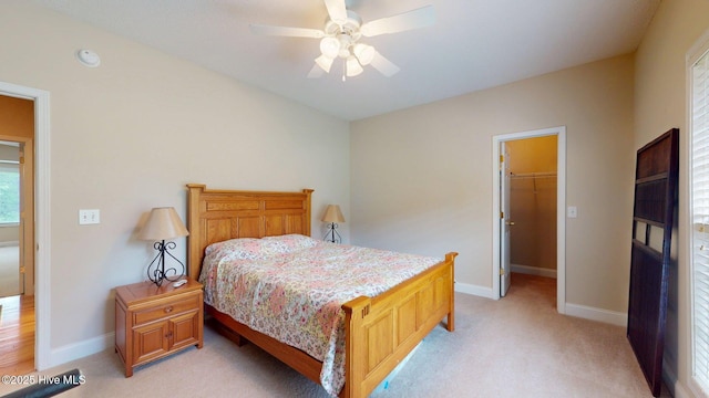 bedroom with a spacious closet, baseboards, a ceiling fan, and light carpet