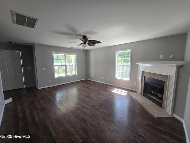 unfurnished living room with plenty of natural light, ceiling fan, dark wood-style flooring, and a premium fireplace