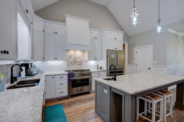 kitchen with white cabinetry, appliances with stainless steel finishes, a sink, and a wainscoted wall
