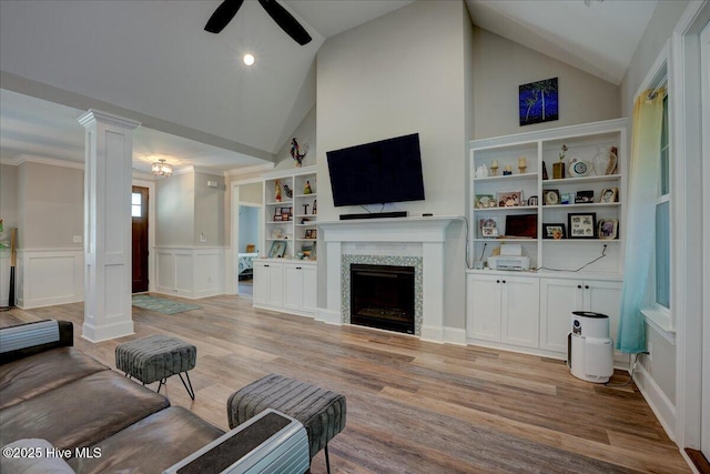 living room with wainscoting, a fireplace, ceiling fan, ornate columns, and light wood-style flooring