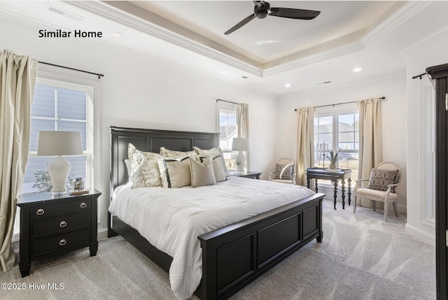 bedroom with a tray ceiling, light colored carpet, and multiple windows