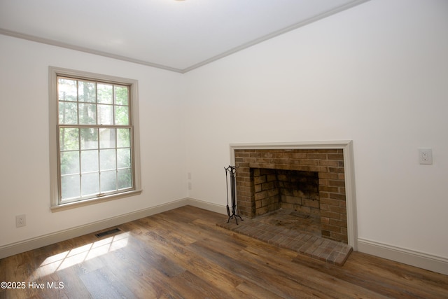 unfurnished living room featuring a brick fireplace, baseboards, visible vents, and wood finished floors