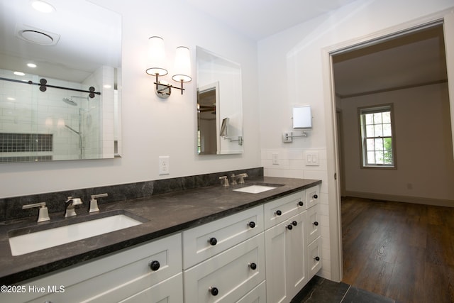 full bath with double vanity, a shower stall, a sink, and wood finished floors