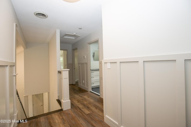 hall featuring an upstairs landing, dark wood-style floors, visible vents, and a wainscoted wall