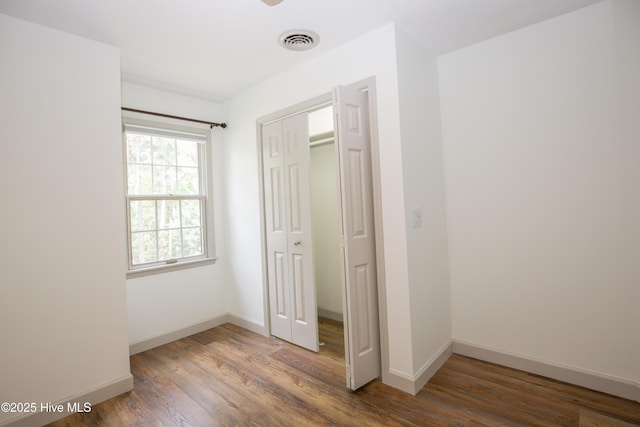 unfurnished bedroom featuring baseboards, a closet, wood finished floors, and visible vents