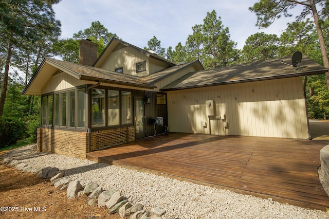 view of front of house featuring a shingled roof, brick siding, a sunroom, a deck, and a chimney