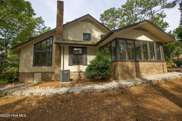 exterior space with a chimney, a sunroom, central AC, and brick siding