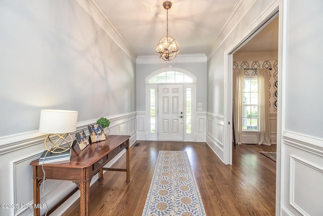 entrance foyer with crown molding, a chandelier, wainscoting, and wood finished floors