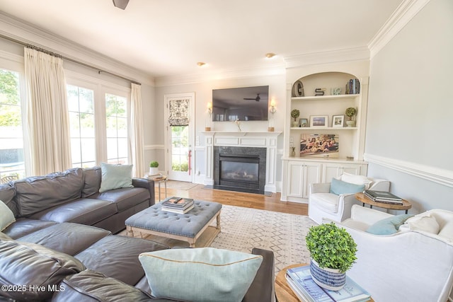 living room with built in shelves, ornamental molding, light wood-style flooring, and a fireplace