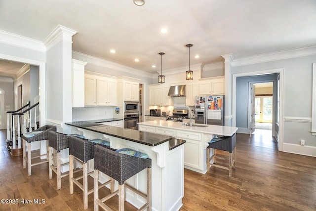 kitchen featuring exhaust hood, a sink, stainless steel appliances, a kitchen bar, and dark wood-type flooring