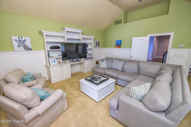 living room featuring light colored carpet, visible vents, lofted ceiling, and a wainscoted wall