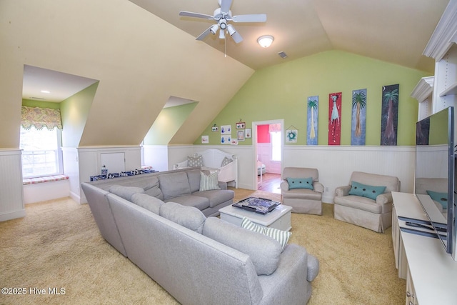 living area with visible vents, light carpet, a wainscoted wall, a ceiling fan, and vaulted ceiling
