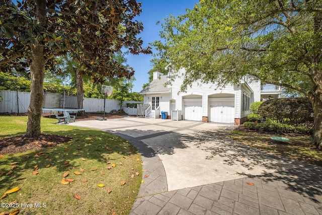 obstructed view of property featuring a garage, fence, a front yard, a trampoline, and driveway