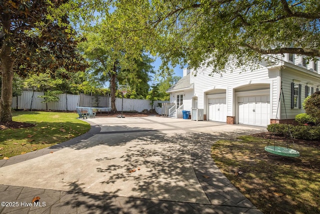 view of front of property featuring fence, a trampoline, a garage, a front yard, and concrete driveway