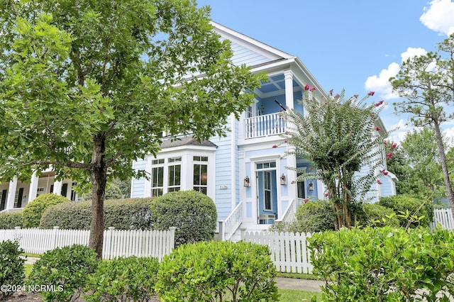 neoclassical / greek revival house featuring a balcony and a fenced front yard