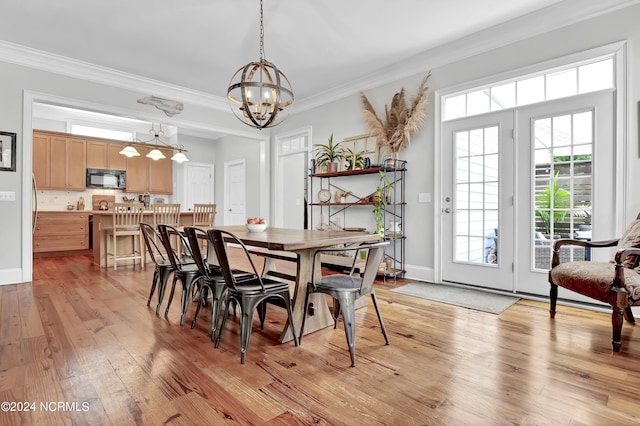 dining space with light wood-style flooring, ornamental molding, a notable chandelier, and baseboards