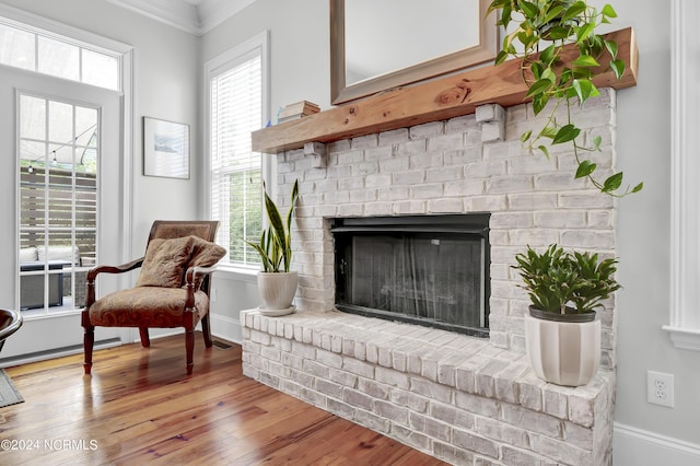 living area with baseboards, wood finished floors, crown molding, and a brick fireplace
