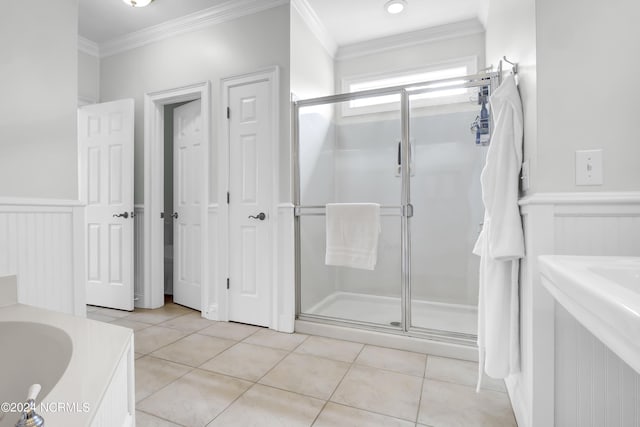 full bath with a shower stall, crown molding, a decorative wall, tile patterned flooring, and wainscoting