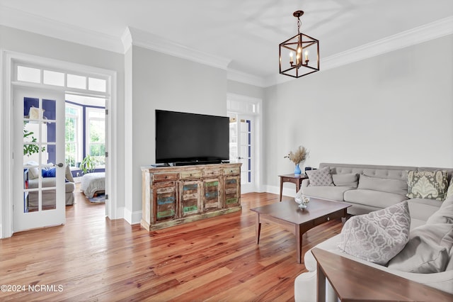 living room with a chandelier, light wood-type flooring, ornamental molding, and baseboards