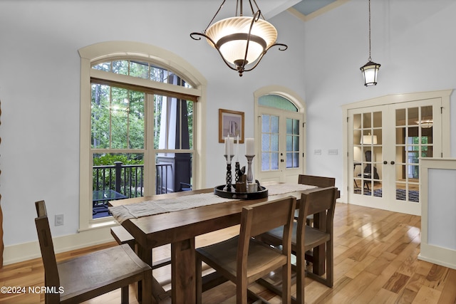 dining area featuring a high ceiling, light wood finished floors, french doors, and an inviting chandelier