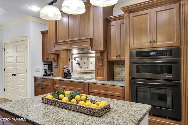 kitchen with a center island, brown cabinets, light stone countertops, black appliances, and tasteful backsplash