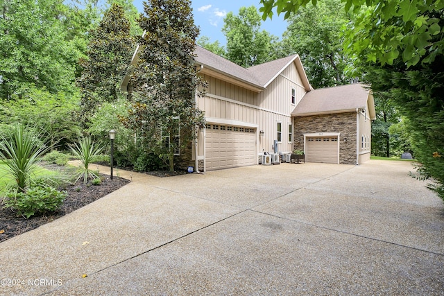 view of side of home featuring roof with shingles, an attached garage, stone siding, driveway, and board and batten siding