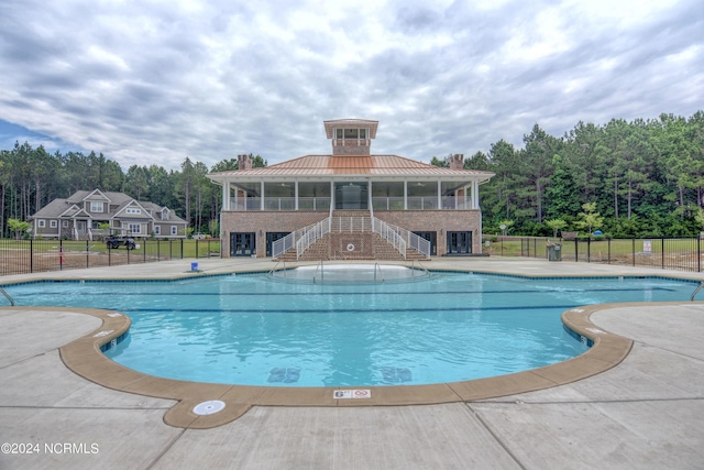 community pool with a patio area, stairway, and fence