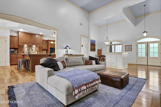 living area featuring crown molding, visible vents, light wood-type flooring, and a high ceiling
