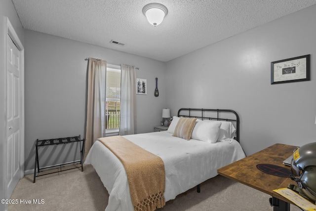 bedroom with a textured ceiling, visible vents, carpet flooring, and a closet
