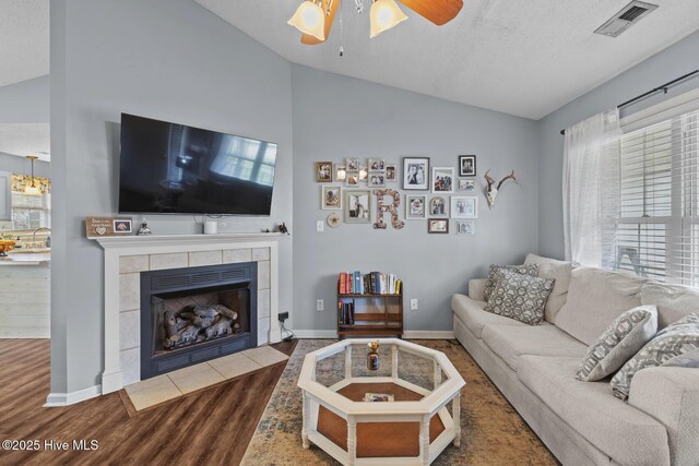 living room with vaulted ceiling, wood finished floors, ceiling fan, a fireplace, and visible vents