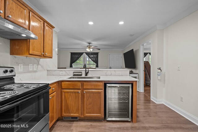kitchen with a sink, beverage cooler, under cabinet range hood, range with electric stovetop, and a peninsula