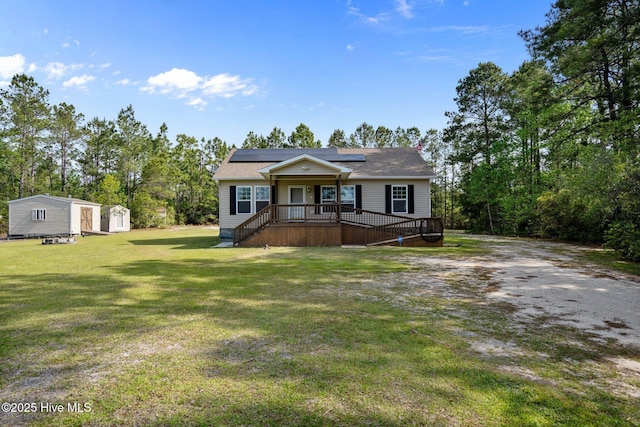 view of front of home with a deck, an outbuilding, solar panels, a shed, and a front yard