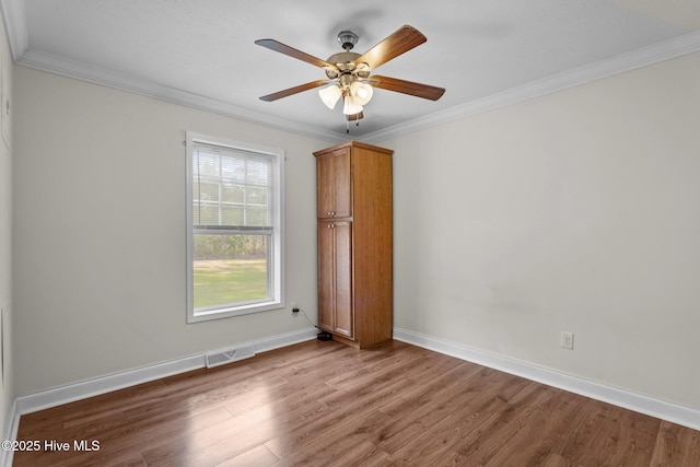 empty room with baseboards, visible vents, wood finished floors, ceiling fan, and crown molding