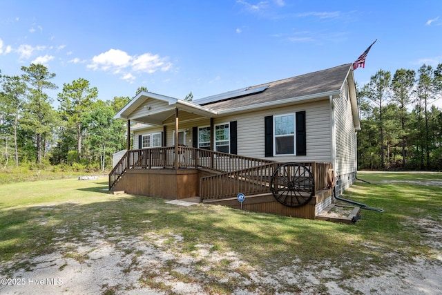 ranch-style house with a shingled roof, covered porch, a front yard, and solar panels