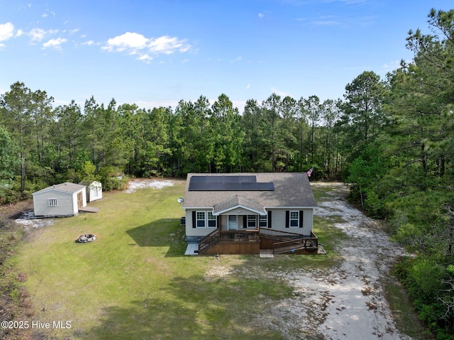 view of front of house with a deck, an outdoor fire pit, solar panels, a front lawn, and a forest view