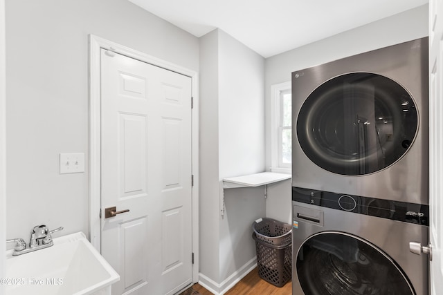 laundry room with wood finished floors, a sink, stacked washer / drying machine, baseboards, and laundry area