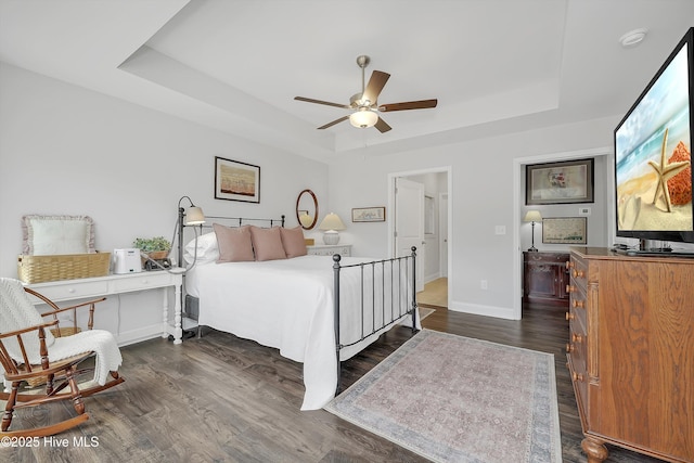 bedroom with a ceiling fan, a tray ceiling, dark wood-style floors, and baseboards