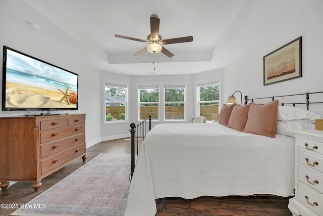 bedroom with baseboards, a ceiling fan, dark wood-style flooring, and a tray ceiling