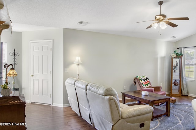 living area with baseboards, visible vents, a ceiling fan, and dark wood-type flooring