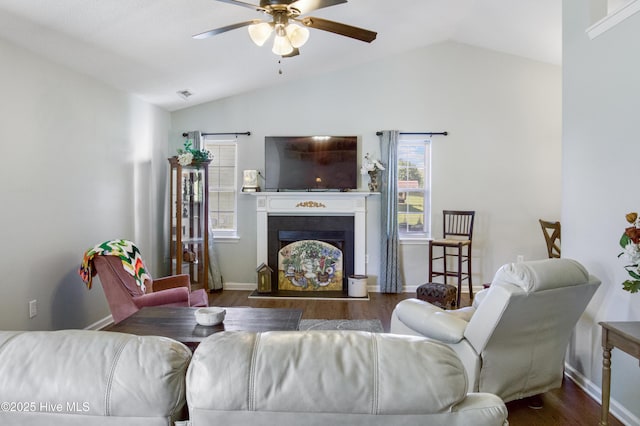 living room featuring a fireplace with raised hearth, a ceiling fan, vaulted ceiling, baseboards, and wood finished floors