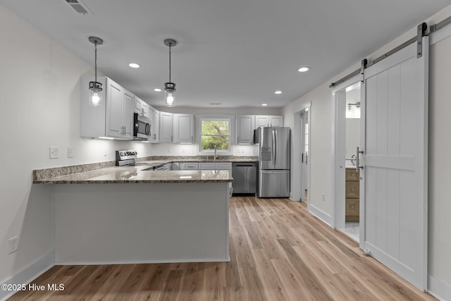 822 N Lord St, Southport, NC 28461 - kitchen featuring dark stone countertops, light wood-style flooring, a barn door, appliances with stainless steel finishes, and a peninsula