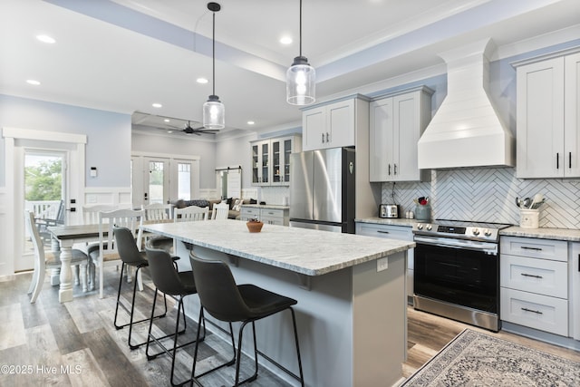 kitchen with decorative backsplash, appliances with stainless steel finishes, a center island, premium range hood, and light wood-style flooring