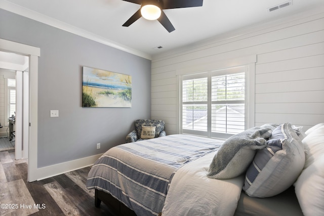 bedroom featuring crown molding, wooden walls, baseboards, visible vents, and dark wood-style floors
