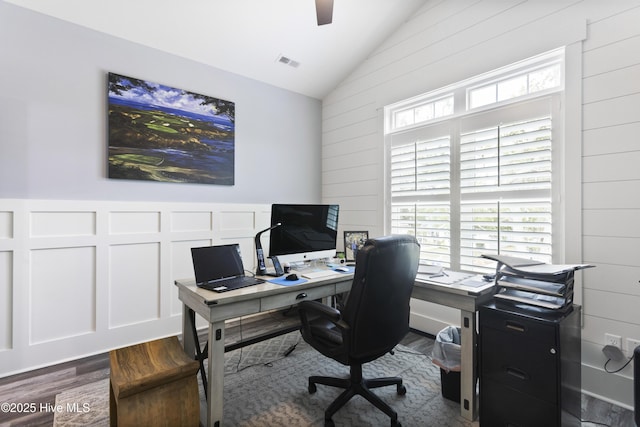 office space featuring a ceiling fan, visible vents, vaulted ceiling, wood walls, and dark wood-type flooring