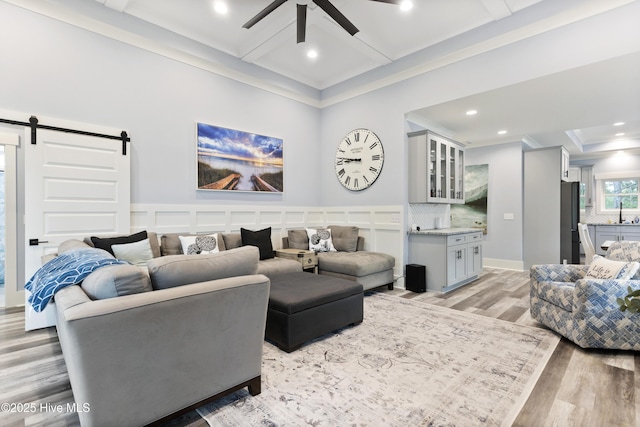 living area with ceiling fan, a barn door, light wood-style flooring, ornamental molding, and coffered ceiling